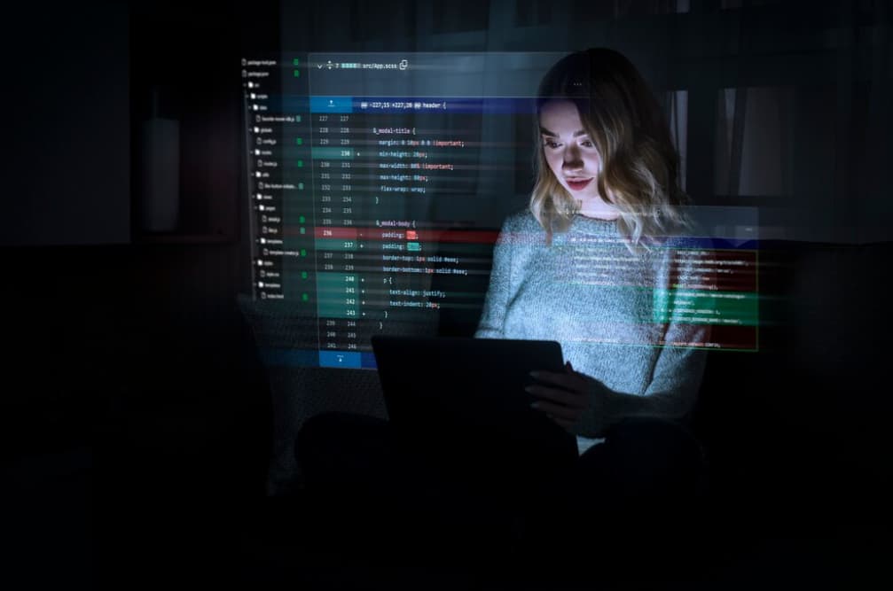 A woman uses a tablet in a dark room with code projected on her face