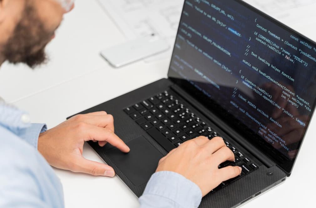 A man typing on a laptop with code on the screen