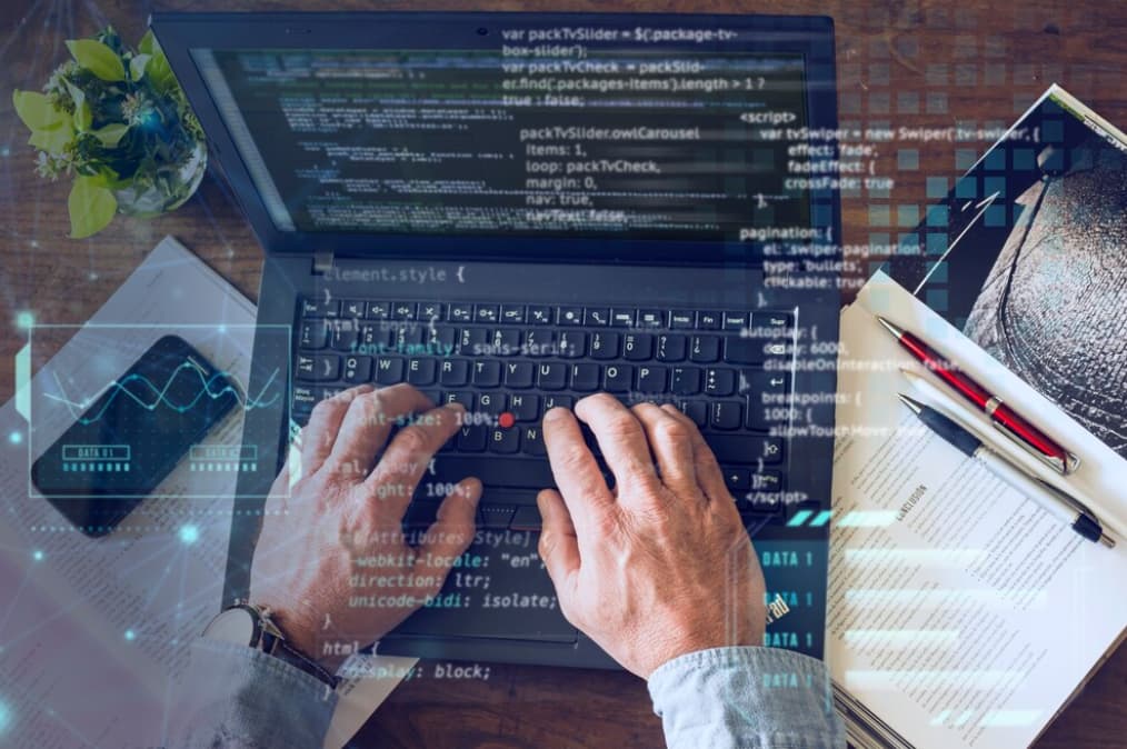 Overhead view of hands typing on a laptop with code and digital data overlay